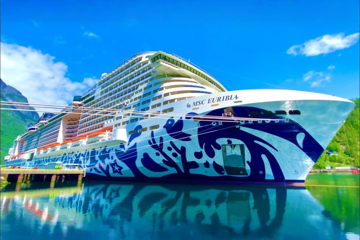 MSC Euribia cruise ship docked in a fjord with green cliffs and blue water, featuring white hull with blue artwork design